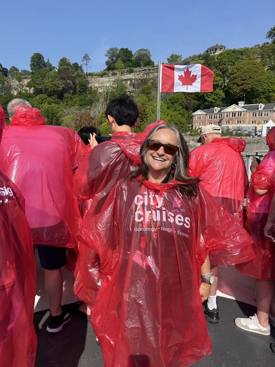 Une visiteuse en imperméable rouge sourit sur le pont du bateau, sous le drapeau canadien
